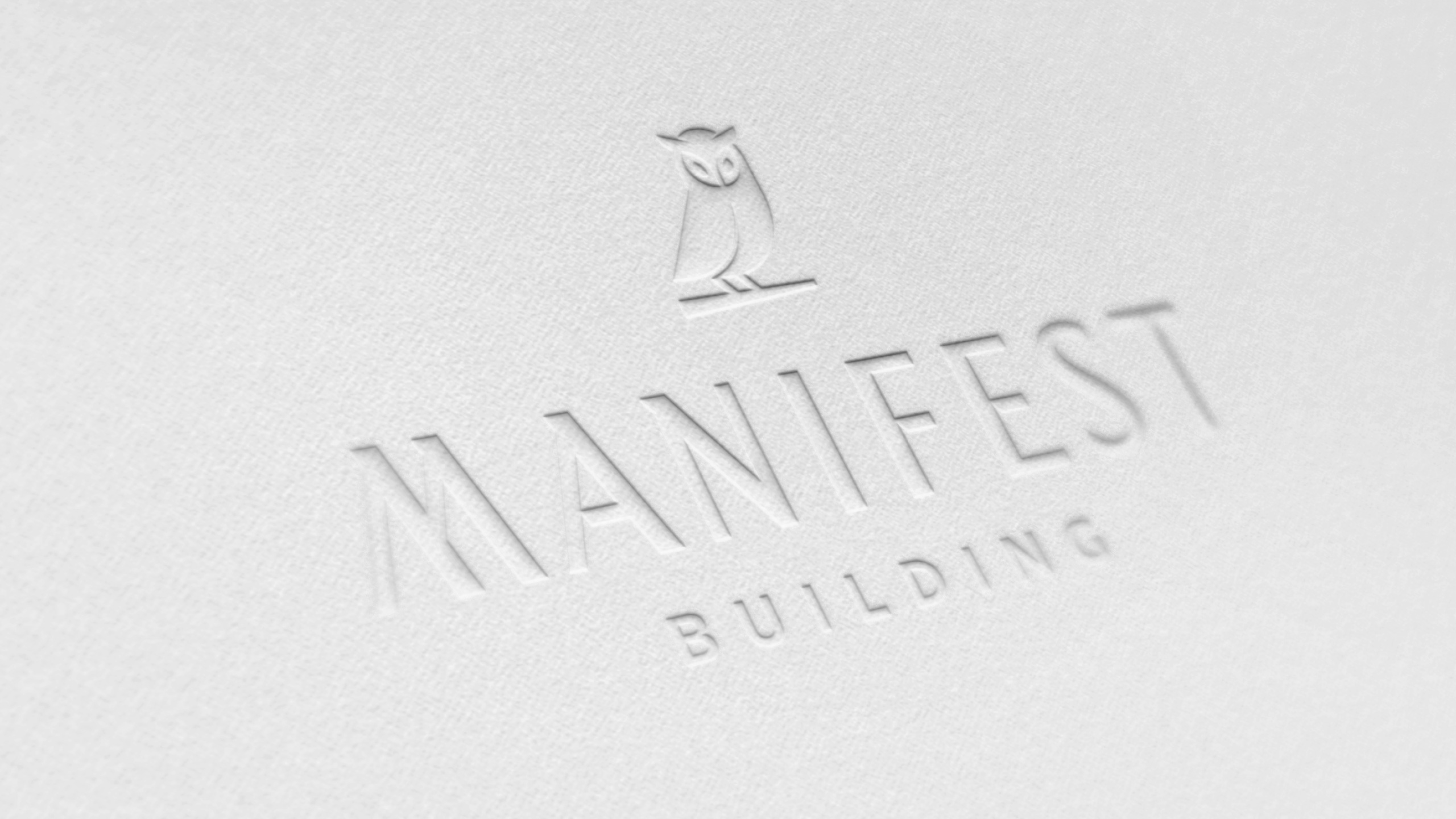 Debossed Manifest Building logo featuring a minimalist owl symbol and elegant typography pressed into textured white paper. Represents the Montecito-based firm's commitment to refined landscape design and craftsmanship in Santa Barbara.
